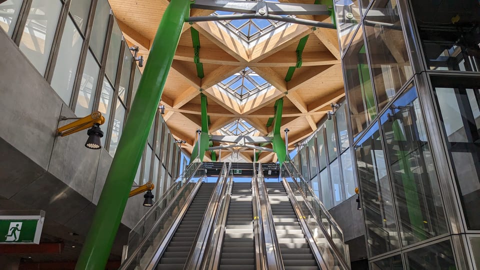 Photo of three escalators leading up to a light-filled wooden ceiling from an underground railway station.