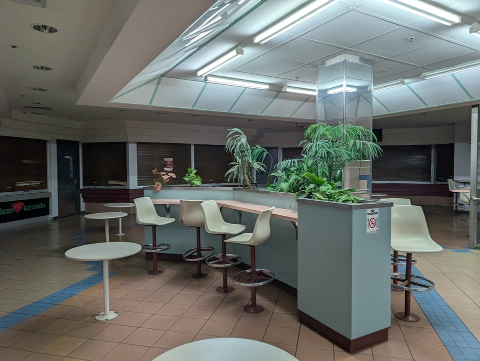 Photo of an empty food court with closed down shops and empty chairs and tables.